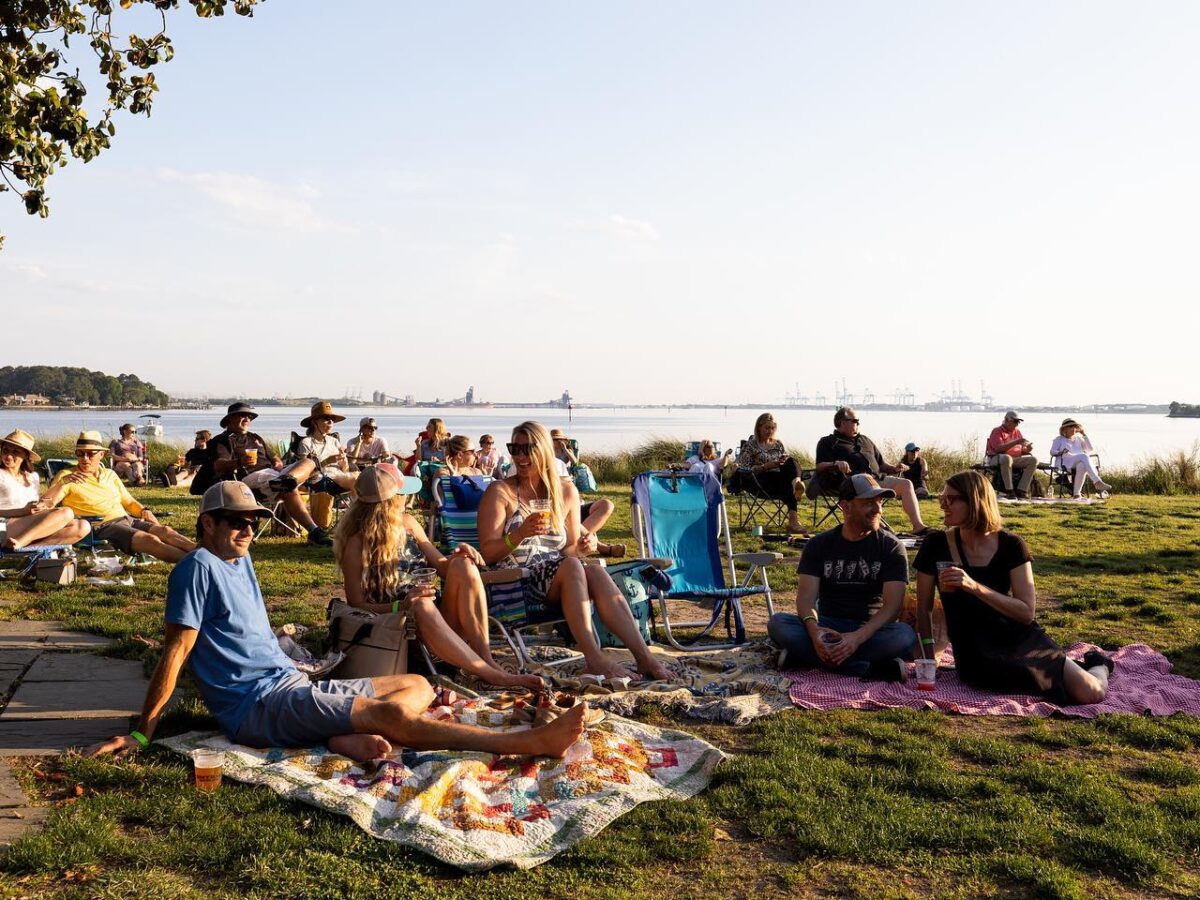 A group of people sitting in chairs and on blankets in front of the water enjoying the sunset